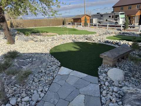 A small chipping green beside a flagstone path and a stone bench, with a larger green behind