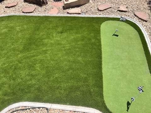 An artificial turf lawn with a putting green set into one side, edged by a concrete curb and flagstone