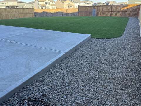 A back lawn of artificial turf beside a new concrete patio and a gravel border, fenced yard