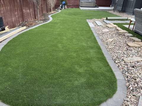 A winding artificial turf lawn with a concrete edge, flagstone set aside and the last of the materials nearby
