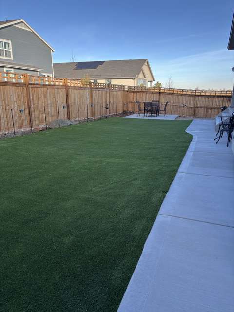 A long side lawn of artificial turf along a concrete walk and cedar fence