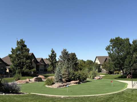 The putting green seen from the street, curving between the lawn, boulders and a concrete path, near Windsor, Colorado